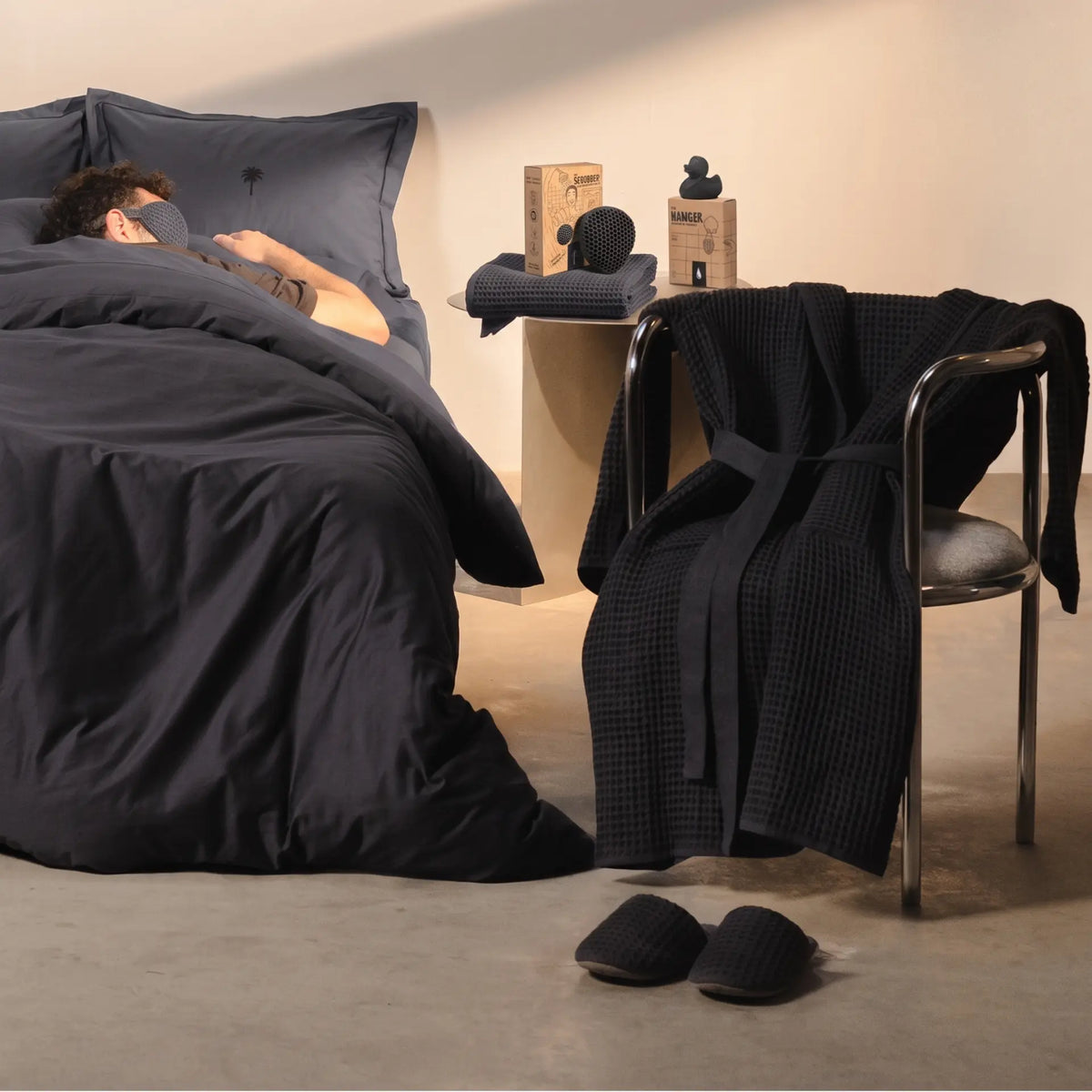 Casamera charcoal sheet set, waffle-weave robe, towels, scrubber and slippers styled in a warm bedroom.